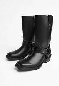 Pair of black leather mid-calf cowboy boots with square toes, harness straps, and low heels on a plain white background.