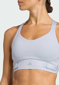 Light grey sports bra with adjustable straps, a soft texture, and an elastic band featuring a logo at the center front under the bust.