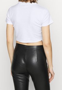 Vit randig kort topp med korta ärmar, matchad med högmidjade svarta läderbyxor. Toppens yta är texturerad och har en kroppsnära passform.