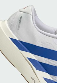 White athletic shoe featuring a textured mesh upper, blue stripes, and a cushioned sole. Notable branding text on the heel.