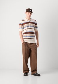 Kortermet polo med beige, brun og blå striper, sammen med brune avslappede bukser og svarte klomper. Enkel design, teksturert stoff.