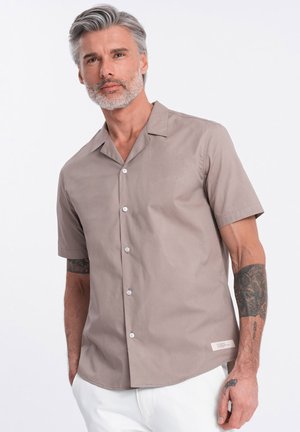 Chemise à manches courtes en tissu taupe clair, avec un col camp, un ourlet droit et des boutons en plastique blanc. Étiquette de marque discrète à l'ourlet.