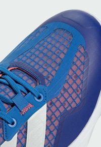 Blue athletic shoe with mesh upper, textured panels, and contrasting red accents. Features blue laces and white detailing on the sole.