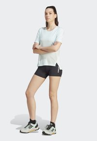 Lys blå kortermet treningsskjorte, svarte shorts med hvit merkevarelogo, og grå fottursko med svarte og gule detaljer.