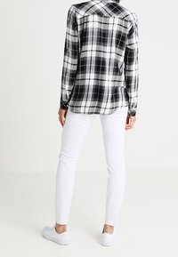 Black and white plaid button-up shirt with long sleeves, paired with white skinny jeans and white sneakers, viewed from behind.
