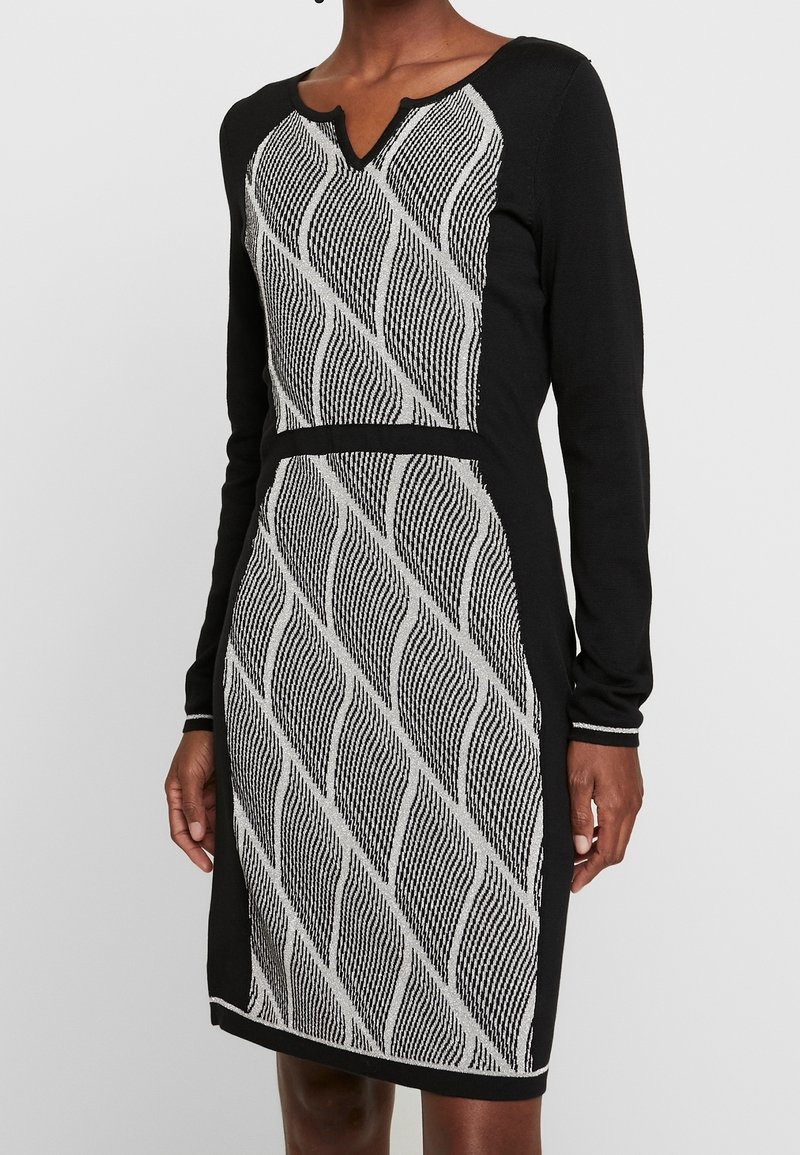 Robe noire à manches longues avec un motif à rayures diagonales ondulées blanches et noires sur le devant et un décolleté légèrement cranté.