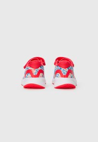 Une paire de baskets pour enfants rouges, blanches et bleues avec des motifs abstraits et des semelles blanches, vue de l'arrière sur un fond uni.
