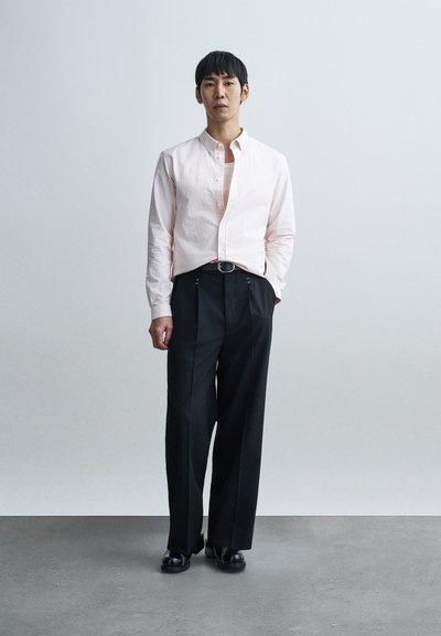 Ανοιχτό ροζ πουκαμίσα με ρίγες, συνδυασμένη με μαύρο παντελόνι φαρδιάς γραμμής, με θηλιές για ζώνη και μεταλλική ζώνη. Μαύρα παπούτσια ολοκληρώνουν την εμφάνιση.