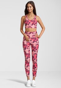 Conjunto de sujetador deportivo y leggings de color rosa con un patrón geométrico en tonos de rosa y burdeos, hecho de tela elástica y con un diseño ajustado.