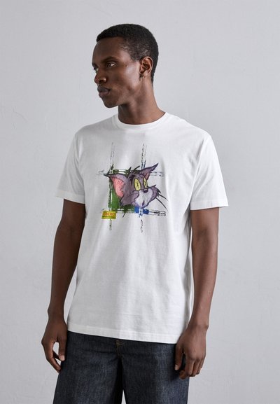 Tricou alb din bumbac, cu o ilustrare a unei pisici de desene animate, având ochi galbeni și urechi roz, conturată cu accente verzi și albastre.