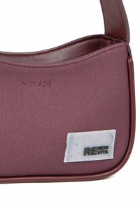 Bordeauxkleurige tas met een structuurstof aan de buitenkant, afgeronde vorm en een leren hengsel. Voorzien van het reliëflogo "MIRIAD" en een gekleurd label.