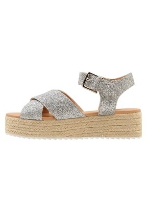 Sølvglitrende espadrille-sandaler med krydsede stropper og justerbar ankelspænde. Mellemsål omgivet af jute; tekstureret ydersål.