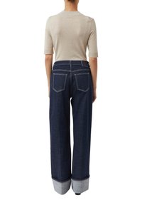 Granatowe jeansy o szerokich nogawkach z wysokim stanem, dużymi tylnymi kieszeniami oraz kontrastującymi jasnoniebieskimi mankietami. Do tego dopasowany, jasnobeżowy top.