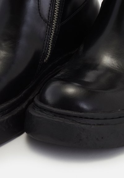 Botas de tobillo de cuero negro con un acabado suave, puntera redondeada y cremallera lateral. Presentan una suela de goma gruesa y texturizada.
