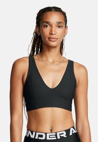Svart randig kort sport-bh med en bred V-ringning och en åtsittande design. Matchas med svarta leggings som visar "UNDER ARMOUR" i vitt.