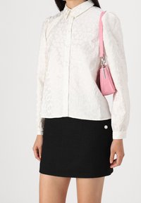 Blouse blanche boutonnée avec motif de cœurs, manches longues et col, associée à une jupe courte noire texturée avec un bouton argenté.