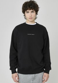 Sweatshirt noir avec texture côtelée et col ras du cou. Comprend du texte blanc "Denmark Street, London UK" au centre à l'avant. Coupe décontractée.