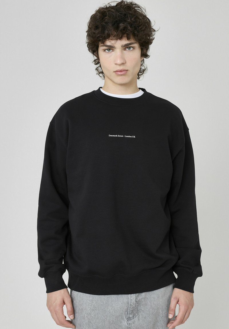 Sweatshirt noir avec texture côtelée et col ras du cou. Comprend du texte blanc "Denmark Street, London UK" au centre à l'avant. Coupe décontractée.