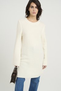 Rochie-pulover de culoare crem, cu un guler rotund și mâneci lungi, asortată cu blugi albaștri și o geantă din piele maro. Țesătură texturată.