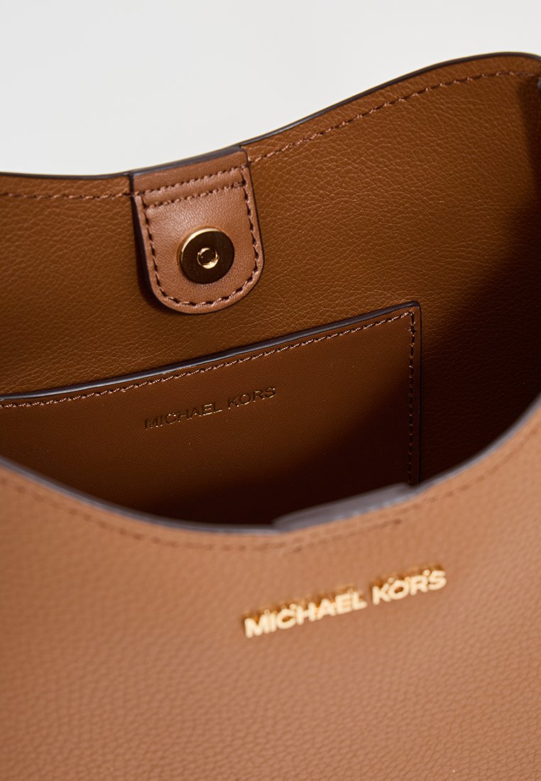 Bruine leren handtas interieur met een gladde textuur, voorzien van een gouden drukknoopsluiting en geperst "MICHAEL KORS" merklogo.