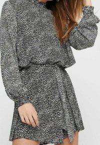 Vestido de lunares en blanco y negro con escote alto, mangas largas abullonadas y cintura ceñida, que presenta una falda acampanada.