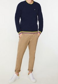 Marinblå stickad tröja med gul krage och randiga muddar, i kombination med beiga avsmalnande byxor. Vita sneakers med gula detaljer.