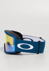 Niebieskie gogle narciarskie Oakley z żółtą lustrzaną soczewką i regulowanym elastycznym paskiem z białym logo Oakley.