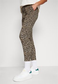 Leggings imprimé léopard en tissu extensible, avec un design ajusté et des poches latérales. Associés à des baskets blanches et des chaussettes blanches.