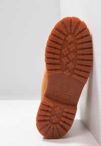 Semelle en caoutchouc brun avec un motif de rainure robuste et le logo Timberland, présentant un bord légèrement surélevé et une finition lisse.