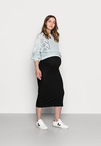 Suéter de malha azul claro com padrão aberto, saia midi justa preta e ténis brancos com detalhes pretos. Design simples e moderno.