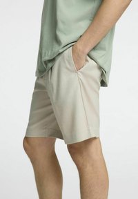 Béžové šortky s texturovanou tkaninou, se bočními kapsami, rovného střihu a jemným leskem, kombinované s světle zeleným topem.