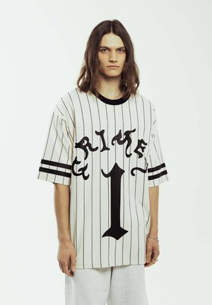 Jersey blanco de gran tamaño con rayas verticales negras, que presenta un gran texto gráfico negro "CRIME" y el número central "1". Mangas cortas, escote redondo.