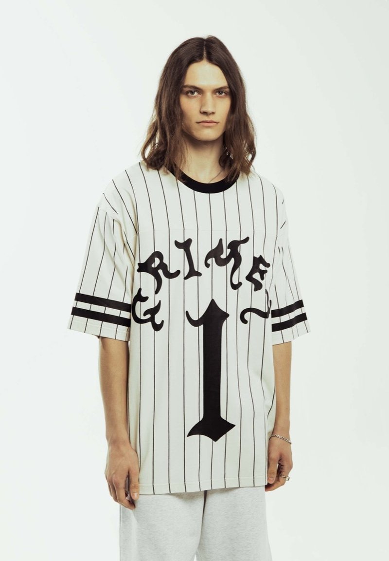 Jersey blanco de gran tamaño con rayas verticales negras, que presenta un gran texto gráfico negro "CRIME" y el número central "1". Mangas cortas, escote redondo.