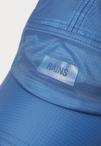 Blue waterproof cap with a smooth, shiny texture. Features a rectangular logo label "RAINS" in a darker blue on the front panel.