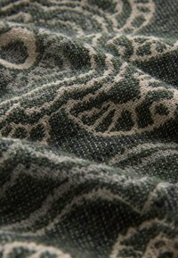 Tuvu pārnestas auduma šķiedras ar zaļām un bēšām izsmalcinātām ziedu un paisleja rakstiem.