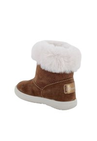 Stivaletto alla caviglia in camoscio marrone con polsino in morbida pelliccia sintetica bianca, suola in gomma bianca e patch con logo dorato sul tallone. Forma compatta, texture soffice.