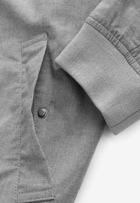 Manga y bolsillo de chaqueta de algodón gris con cierre de botón a presión, mostrando costuras detalladas y textura de puño acanalado.