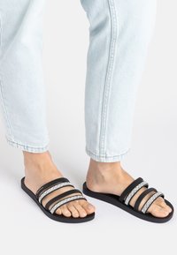 Schwarze Rutsch-Sandalen mit drei breiten Riemen, von denen zwei mit silbernen Akzenten verziert sind, strapazierfähige Gummisohle und minimalistisches Design.
