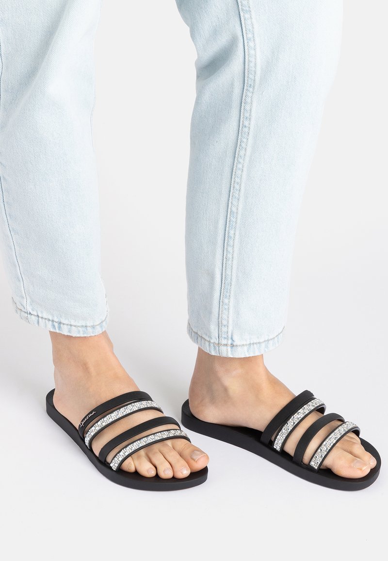 Schwarze Rutsch-Sandalen mit drei breiten Riemen, von denen zwei mit silbernen Akzenten verziert sind, strapazierfähige Gummisohle und minimalistisches Design.