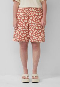 Shorts rosa con un motivo astratto leopardato color crema, dotati di una vita elastica e cordoncino. Indossati con sandali con piattaforma di colore chiaro.