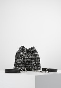Sac seau en tissu tissé noir et blanc avec des accents en chaîne argentée, bandoulière en cuir réglable et fermeture à cordon.