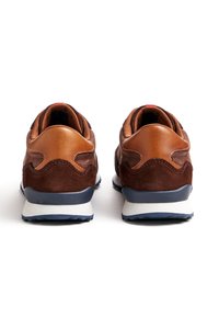 Paar braune und beige Wildleder-Sneaker aus der Rückansicht, mit gepolsterten Kragen, weißen Zwischensohlen und dunkelblauen Außensohlen auf weißem Hintergrund.