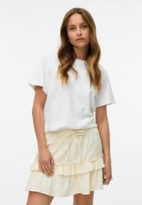 T-shirt blanc à manches courtes associé à une jupe volantée jaune clair avec taille à cordon, mettant en valeur un tissu texturé.