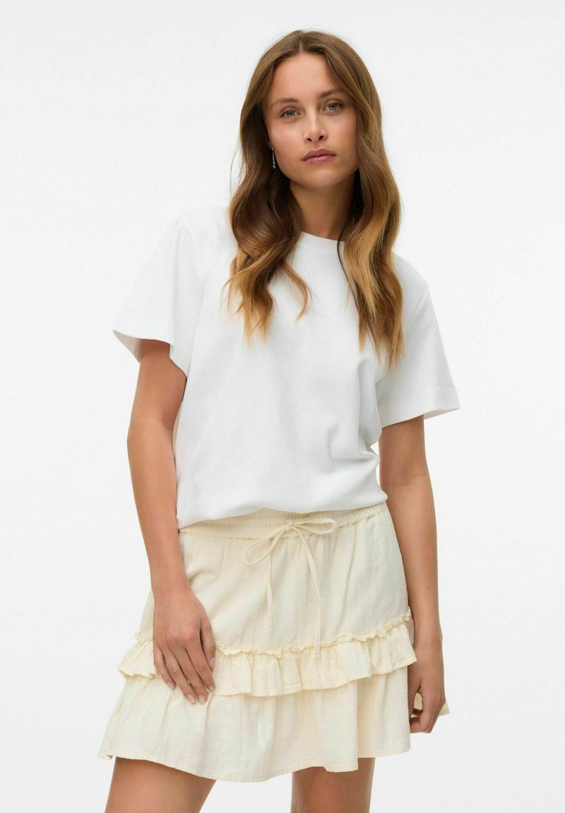 T-shirt blanc à manches courtes associé à une jupe volantée jaune clair avec taille à cordon, mettant en valeur un tissu texturé.