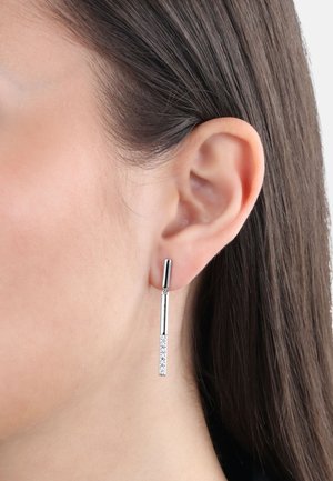 Srebrne kolczyki w kształcie kropli o eleganckim designie. Górna część ma cylindryczny kształt, połączona z dłuższym prętem, na którym znajduje się rząd małych, przezroczystych kryształków.