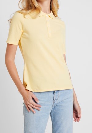 Geel polo shirt van katoen, met een kraag, korte mouwen en een vijfknops knoopsluiting. Gepaarde met lichtblauwe denim jeans.