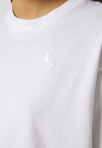 T-shirt en coton blanc avec un col rond. Il possède un petit logo Jumpman brodé sur la partie gauche de la poitrine. Texture lisse.