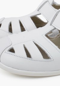 Sandali bianchi in pelle caratterizzati da un design a ritagli, cinturini regolabili e un interno morbido. Texture liscia con dettagli di cucitura in contrasto.