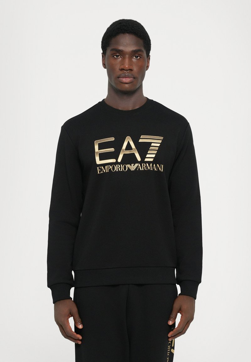 Svart hettegenser med et gulllogo "EA7 EMPORIO ARMANI" på forsiden, med ribbede mansjetter og rund halslinning. Myk stoffkvalitet.