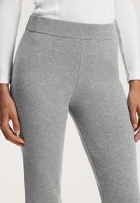 Sive pletene legice z širokim, rebrastim pasom. Tkanina ima mehak občutek in rahlo elastičnost. Poudarjen je ozek pogled na pas in zgornji del noge.